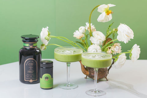 Matcha Tea in glass stemware on table with flower, by Magic Hour