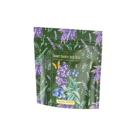 A green metallic tea packaging with colorful illustrations of lavender, mint leaves, a butterfly, and blueberries. It reads "Blueberry Lavender Mint: Cosmic Garden Iced Tea." The brand "Magic Hour" is prominently displayed at the bottom of the pouch.