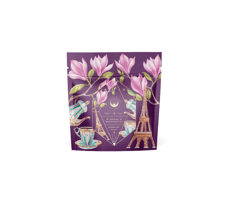 A purple tea package adorned with an illustration of pink flowers, teacups, a teapot, and the Eiffel Tower evokes a romantic interlude. The standout design features a diamond-shaped emblem with celestial symbols and the text "Breakfast in Paris - Oolong Black Tea Scented with Fruits & Flowers of Secret Parisian Gardens.