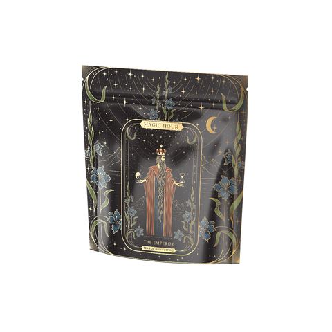 A black packaging bag showcasing a tarot card design labeled "The Emperor," featuring a robed, crowned figure with outstretched hands, encircled by an elaborate celestial-themed border adorned with stars, moons, and floral elements. Ideal for inclusion in your Monthly Magic First Sips Tea Subscription Box from Magic Hour Medicinal Herbal Wellness Teas.