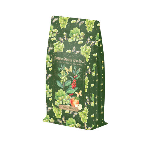 A green package of Green Grape Yerba Mate: Cosmic Garden Iced Tea from Magic Hour. The design features illustrations of green grapes, honeybees, and apple slices on a dark green background, giving it a natural and whimsical look. Enjoy this delightful organic tea in loose leaf form.