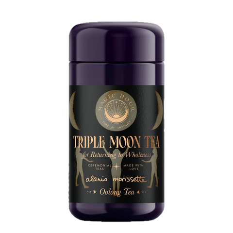 A purple cylindrical container labeled "Triple Moon Tea by Alanis Morissette to Celebrate her Triple Moon Tour!" with gold accents. The label features text "for Returning to Wholeness," "Ceremonial teas," "Made with love," and "Magnolia Oolong Tea" along with crescent moon designs and a central logo reading "Magic Hour.