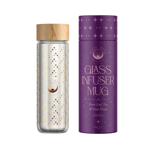 A double-walled borosilicate glass infuser mug with a wooden lid adorned with a celestial design of stars and moons sits next to its matching purple cylindrical packaging. The packaging, labeled Glass Infuser Mug for Loose Leaf Tea & Fruit Water," features a starry pattern that complements the mug's design.