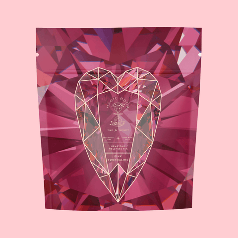 The "Pink Tourmaline Bath Soak" package showcases a geometric heart design set against a faceted, gem-like pink background. The packaging, labeled "Magic Hour," highlights the product benefits on the front, mentioning "time & energy," "wellness tea," and "tourmaline." This bath soak is infused with organic tea seed oil.