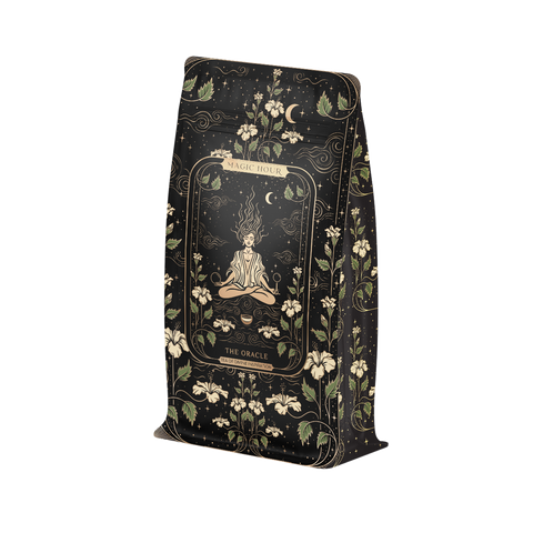 A black pouch with an intricate design contains Magic Hour's "The Oracle: Lemon Lavender Tea for Supporting the Gut-Brain Axis Case Packs." This caffeine-free blend features a meditating figure surrounded by flowers, celestial symbols, and ornate patterns. Infused with adaptogenic roots, the packaging also showcases white floral and vine elements in the background.