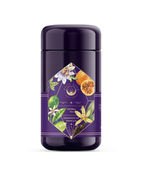 A cylindrical purple canister labeled "Romance in Ravello - Chocolate-Passionfruit-Rose-Cream White Tea" from "Magic Hour." The packaging features geometric and floral designs with images of passionflowers and other botanical elements, evoking the charm of the Amalfi Coast with a delightful passion fruit blend.