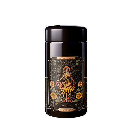 A black tea tin labeled "Magic Hour" featuring the design "The Sun." The tin showcases a vibrant illustration of a woman in a flowing dress, surrounded by sunflowers and celestial elements, with hints of Moringa. The phrase "Tea for Prosperity" is inscribed at the bottom.