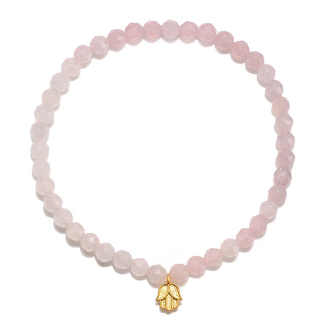 The Rose Quartz Mini Hamsa Bracelet features translucent pink Rose Quartz beads arranged in a circular pattern, highlighted by a small golden Hamsa hand charm that prominently hangs at the bottom center. The background is plain white.