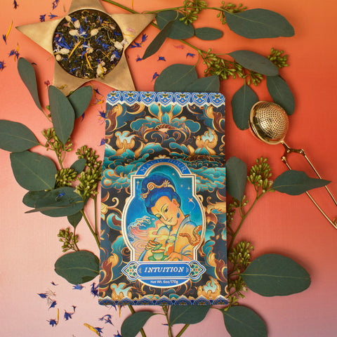 A box of Magic Hour's Nuwa Tea for Intuition: Dragon Yuzu Oolong Case Packs, adorned with intricate artwork of a meditative figure, is surrounded by green leaves, small purple flowers, a tea infuser, and loose Taiwanese Tung Ting-Dragon Oolong on a gradient orange-to-pink background.