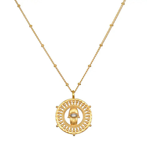 The Palm of Protection Hamsa Coin Necklace is a gold necklace showcasing a circular pendant with an intricate openwork design. At its center is an eye motif highlighted by a labradorite gemstone, and the thin chain is embellished with small, evenly spaced beads.