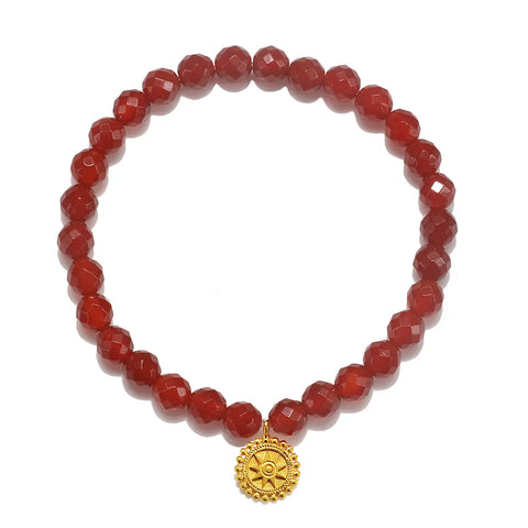 The Red Carnelian Mandala Bracelet consists of round, faceted red beads and showcases a gold circular pendant adorned with an intricate sunburst design. This gemstone bracelet is perfectly arranged in a circle, capturing the essence of healing jewelry.