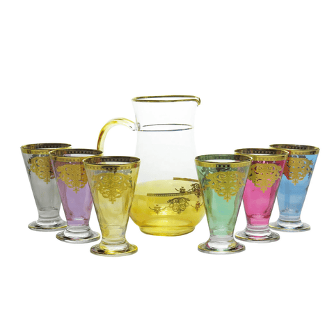 The Romantic Tea Set - Six Glasses & Pitcher features a clear glass pitcher with a yellow handle and base, adorned with an elegant gold floral pattern inspired by classic Italian design. Accompanying the pitcher are six matching glasses in a variety of colors—yellow, purple, green, blue, pink, and gray—each embellished with gold floral designs near the rims. Perfect for adding a romantic touch to your tea time.