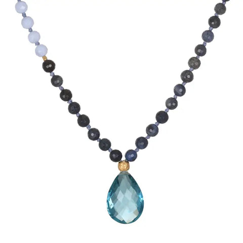 A Magic Hour Wise Spirit Sky Blue Topaz Gemstone Drop Mala with alternating dark-colored and light blue beads, featuring a large, teardrop-shaped, faceted blue topaz gemstone pendant at the center, connected by two small golden beads.