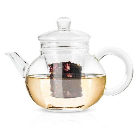 The Hand Blown 32oz Glass Teapot with Infuser has a transparent, round body complete with a handle, spout, and lid. Crafted from heat-resistant borosilicate glass, this teapot includes a removable glass infuser basket. Hibiscus tea leaves steep inside the light yellow liquid, clearly visible through the glass.